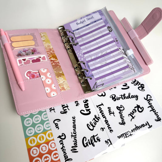 Pink planner with stickers and a pen on a white background